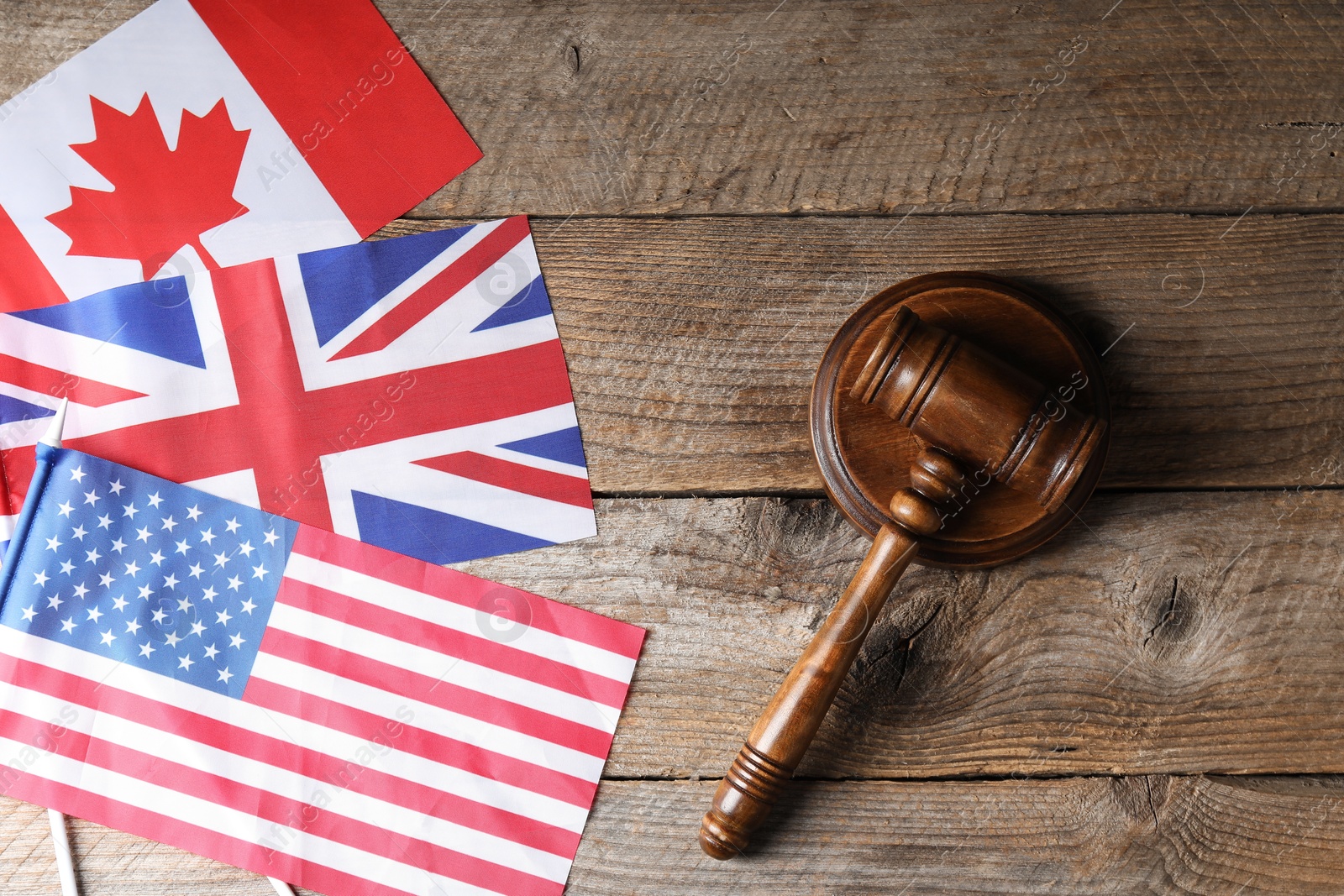 Photo of Judge's gavel and flags of USA, United Kingdom and Canada on wooden table, top view