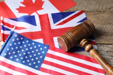 Photo of Judge's gavel and flags of USA, United Kingdom and Canada on wooden table, closeup