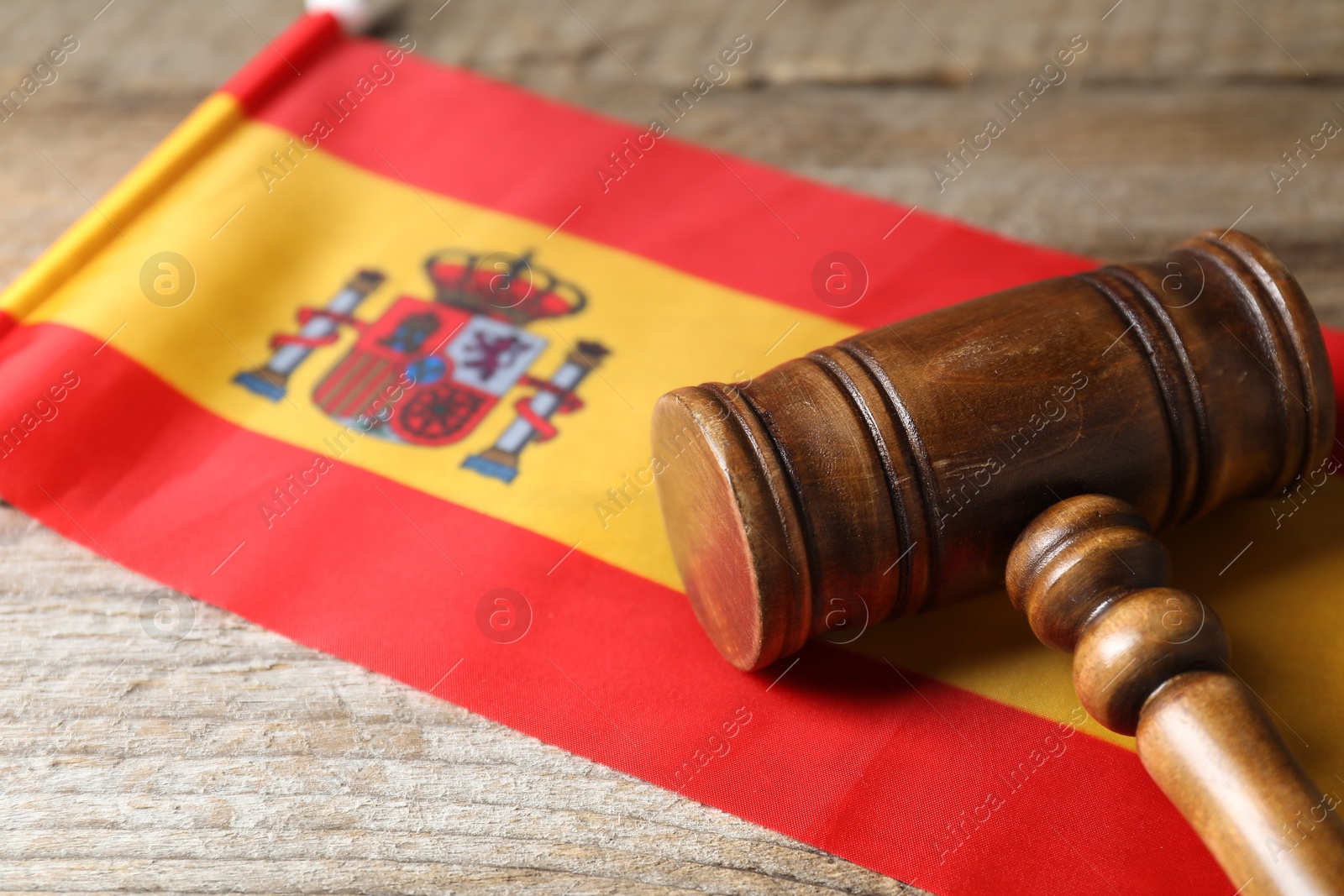 Photo of Judge's gavel and flag of Spain on wooden table, closeup