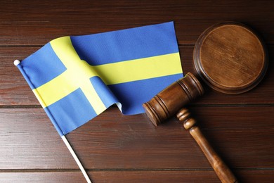 Photo of Judge's gavel and flag of Sweden on wooden table, top view