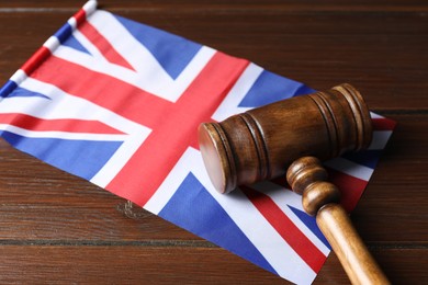 Photo of Judge's gavel and flag of United Kingdom on wooden table, closeup