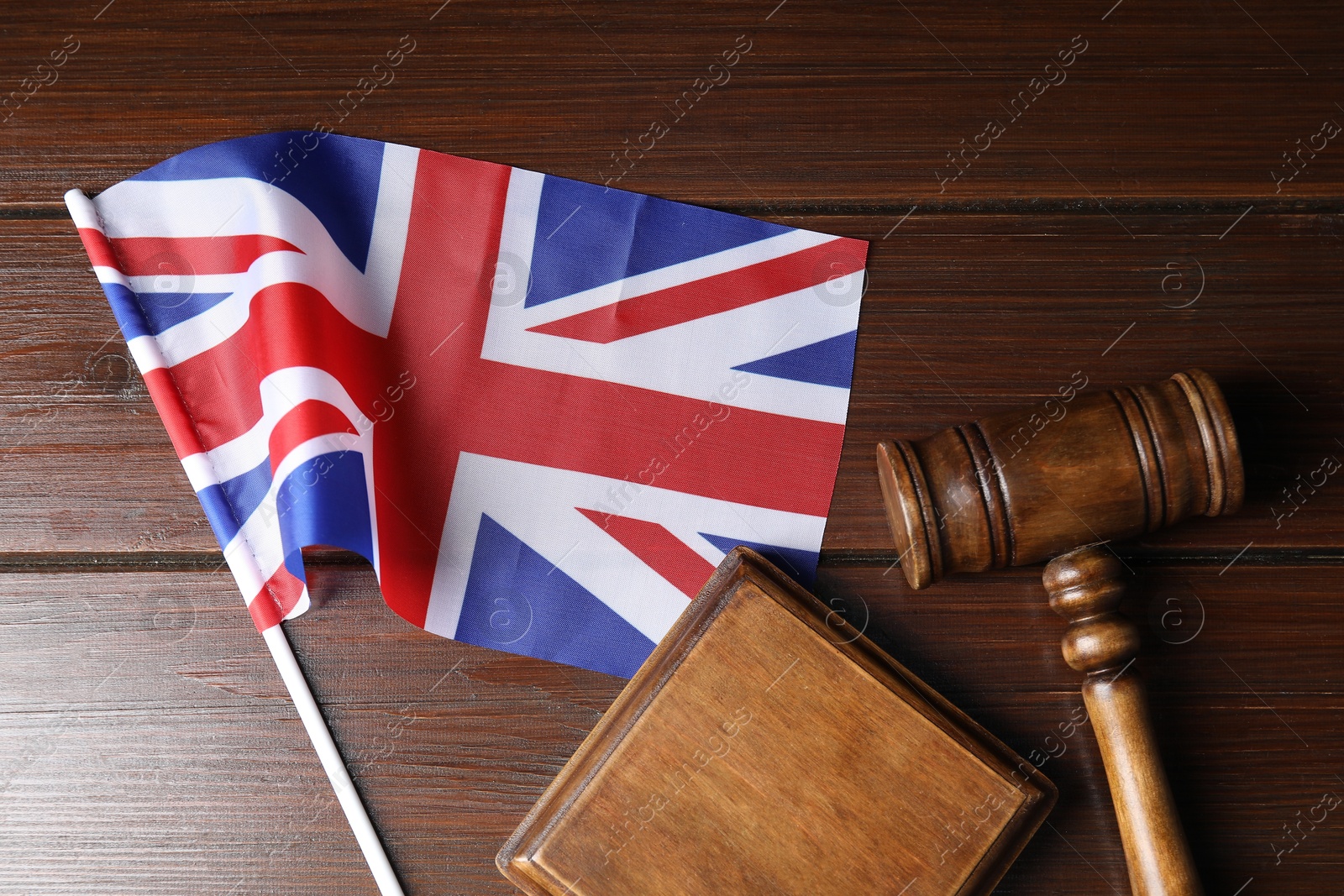 Photo of Judge's gavel and flag of United Kingdom on wooden table, top view