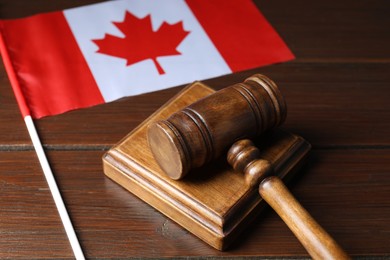 Photo of Judge's gavel and flag of Canada on wooden table, closeup