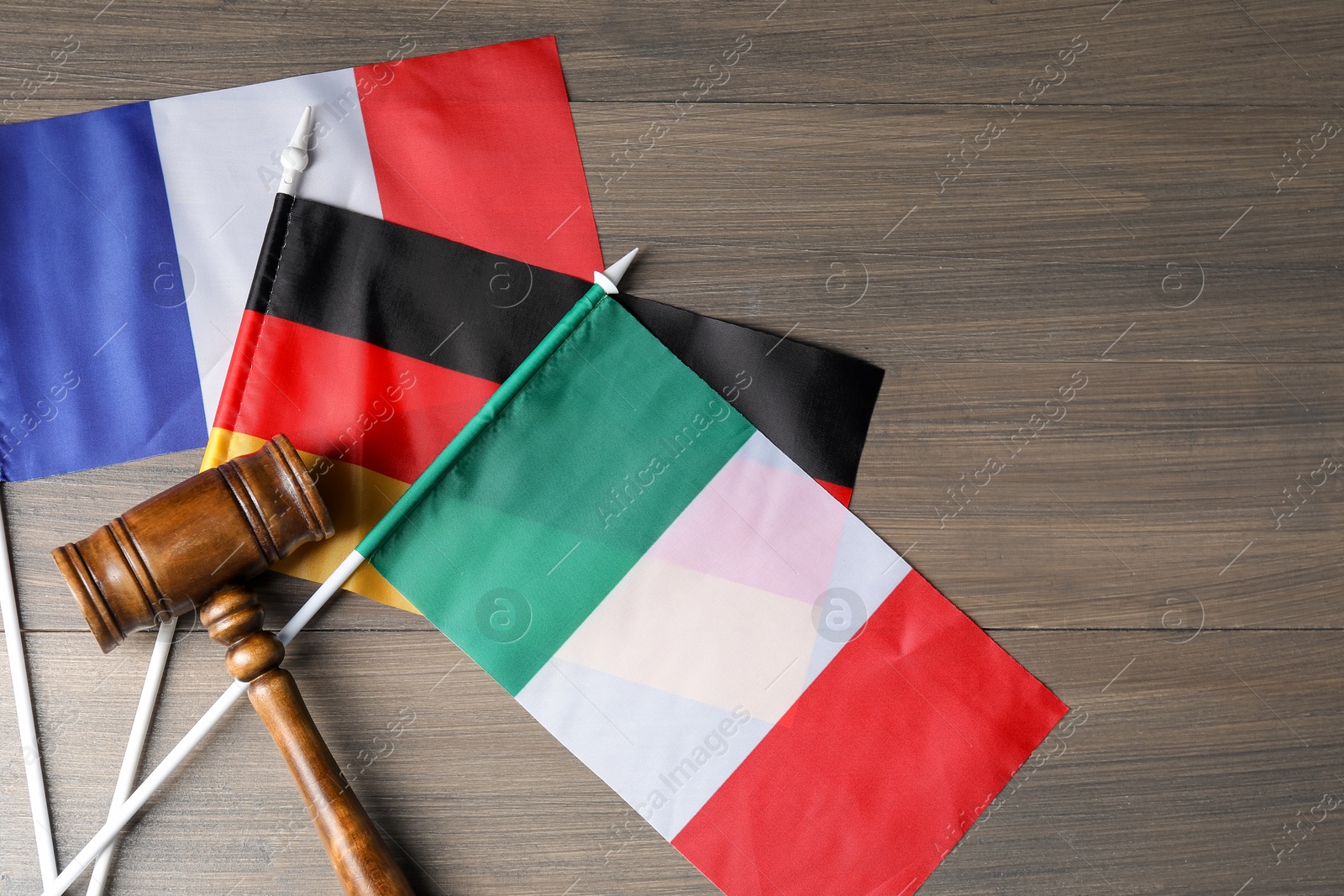 Photo of Judge's gavel and flags of Italy, Germany and France on wooden table, top view
