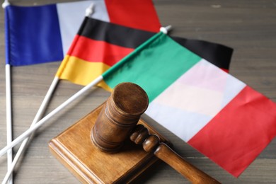Photo of Judge's gavel and flags of Italy, Germany and France on wooden table, closeup