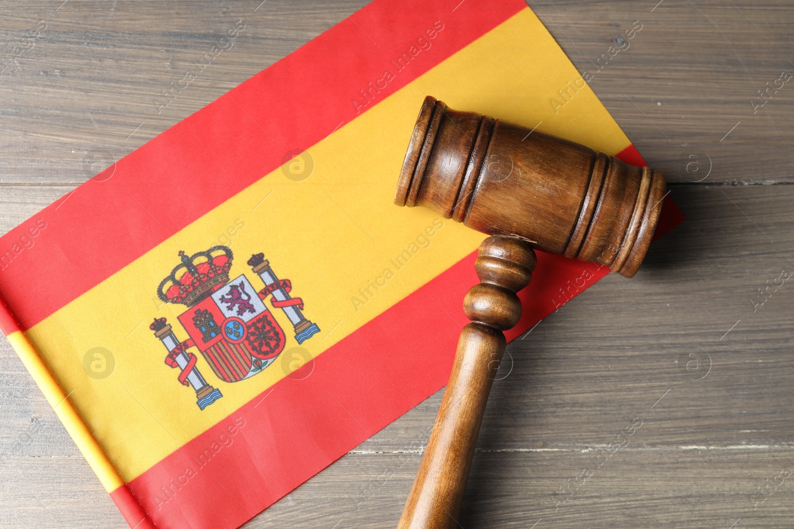 Photo of Judge's gavel and flag of Spain on wooden table, top view
