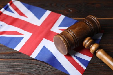 Photo of Judge's gavel and flag of United Kingdom on wooden table, closeup