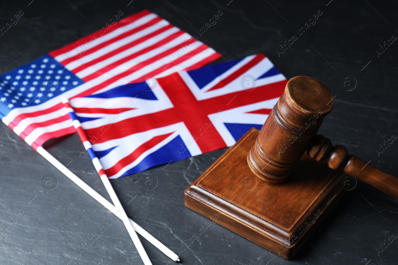 Photo of Judge's gavel and flags of USA and United Kingdom on black table, closeup