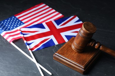 Photo of Judge's gavel and flags of USA and United Kingdom on black table, closeup