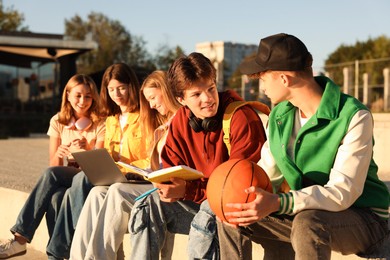 Photo of Group of teenagers doing homework together outdoors, selective focus
