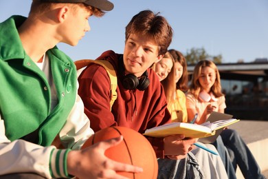 Photo of Group of teenagers doing homework together outdoors, selective focus