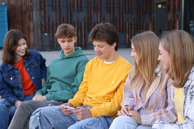 Photo of Group of teenagers watching something on smartphone outdoors