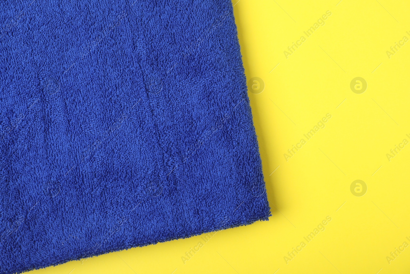 Photo of Blue terry towel on yellow background, top view. Space for text