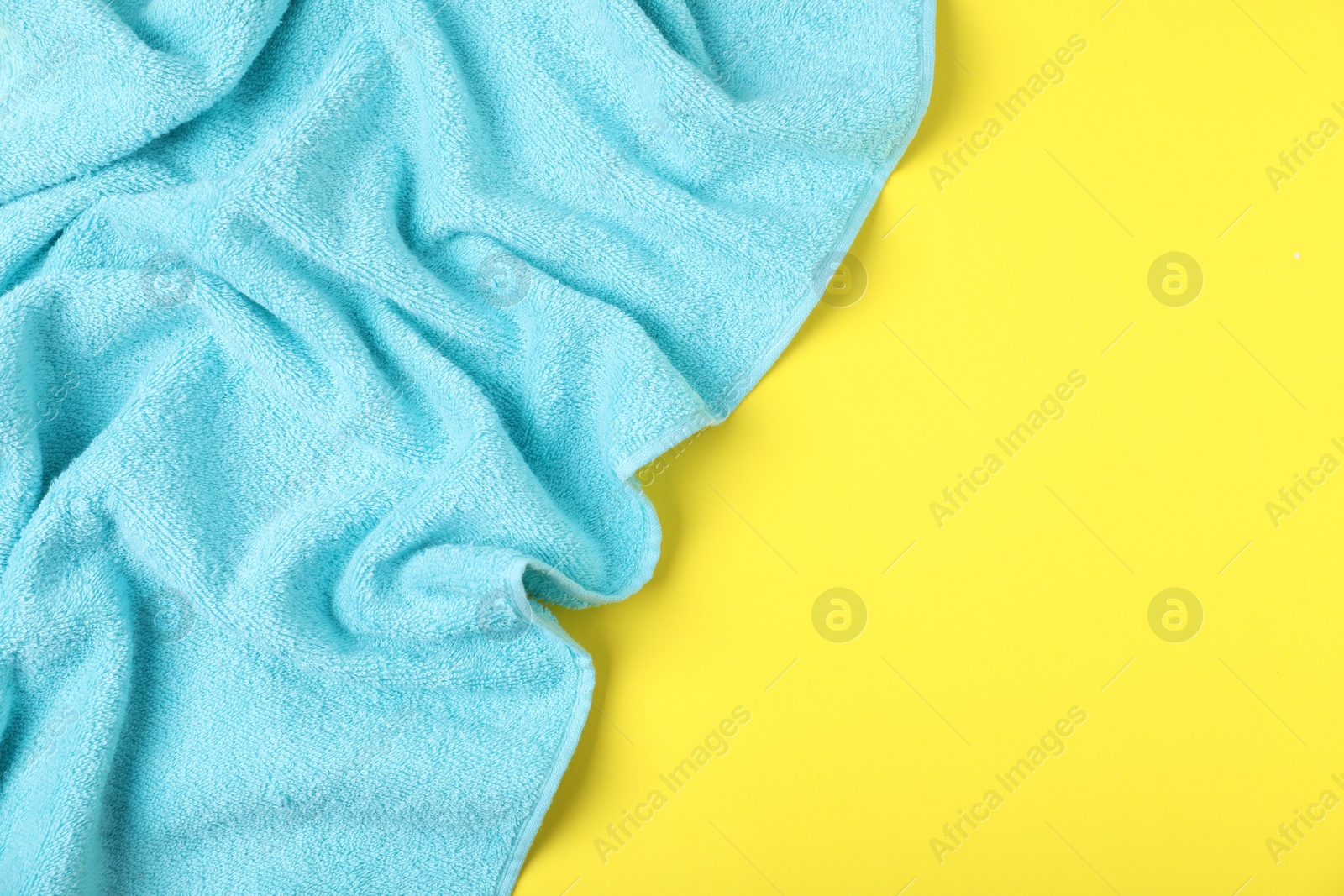 Photo of Light blue terry towel on yellow background, top view. Space for text