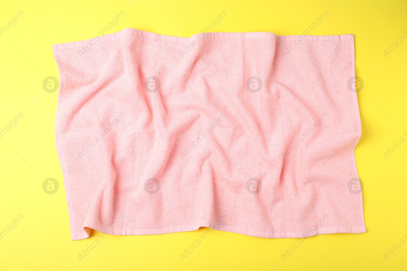 Photo of Pink terry towel on yellow background, top view