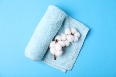 Photo of Clean terry towel and cotton flowers on light blue background, top view