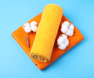 Photo of Clean terry towels and cotton flowers on light blue background, above view