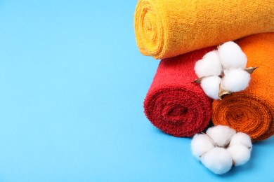 Photo of Clean terry towels and cotton flowers on light blue background, closeup. Space for text