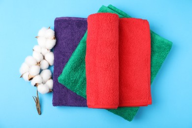 Photo of Bright terry towels and cotton flowers on light blue background, flat lay