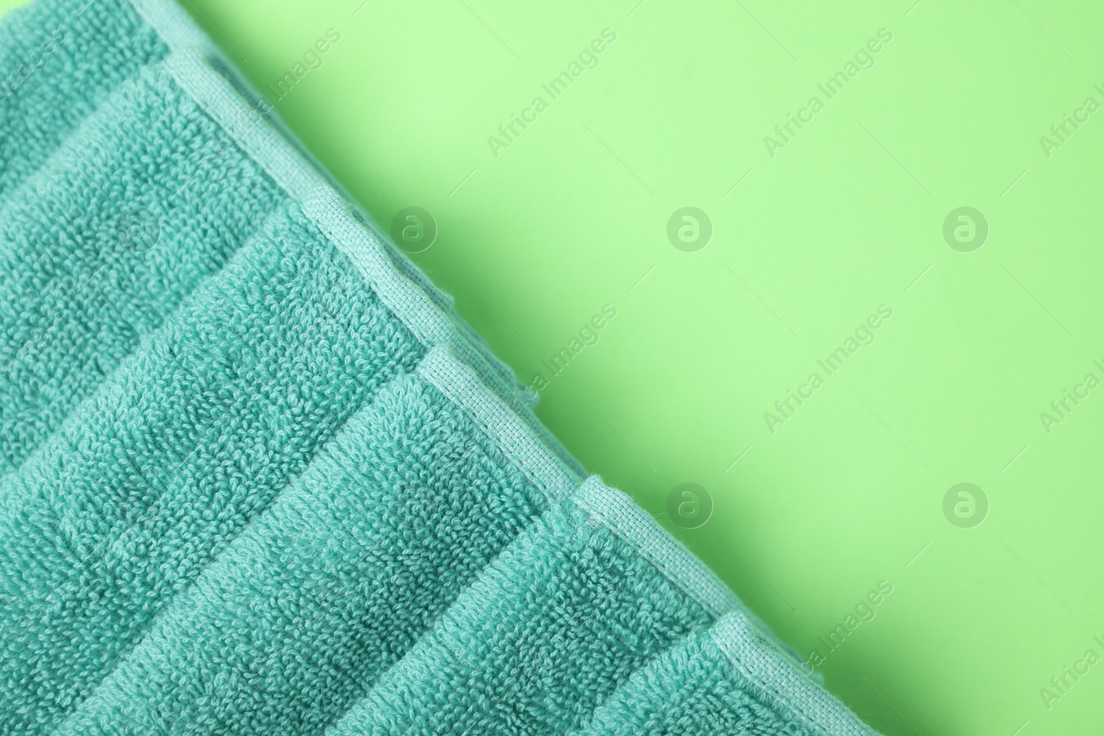 Photo of Turquoise terry towel on green background, top view. Space for text