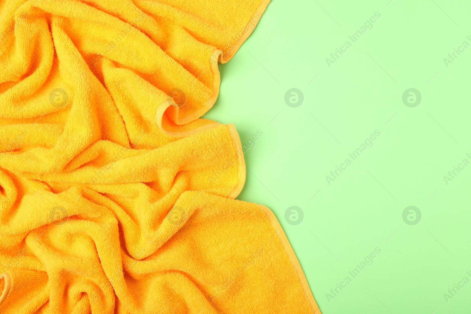Photo of Yellow terry towel on green background, top view. Space for text