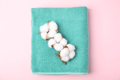 Photo of Turquoise terry towel and cotton flowers on pink background, top view