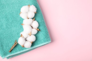Photo of Turquoise terry towel and cotton flowers on pink background, top view. Space for text