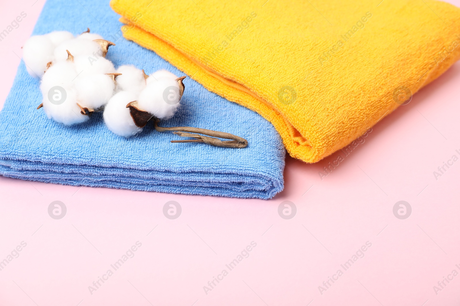 Photo of Bright terry towels and cotton flowers on pink background, closeup. Space for text