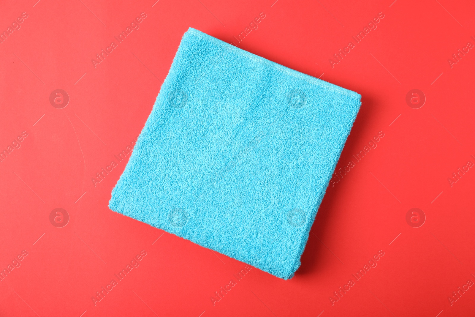 Photo of Light blue terry towel on red background, top view