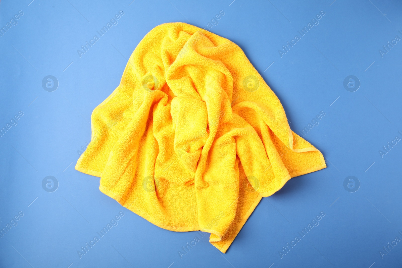 Photo of Yellow terry towel on blue background, top view