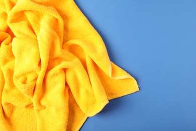 Photo of Yellow terry towel on blue background, top view. Space for text
