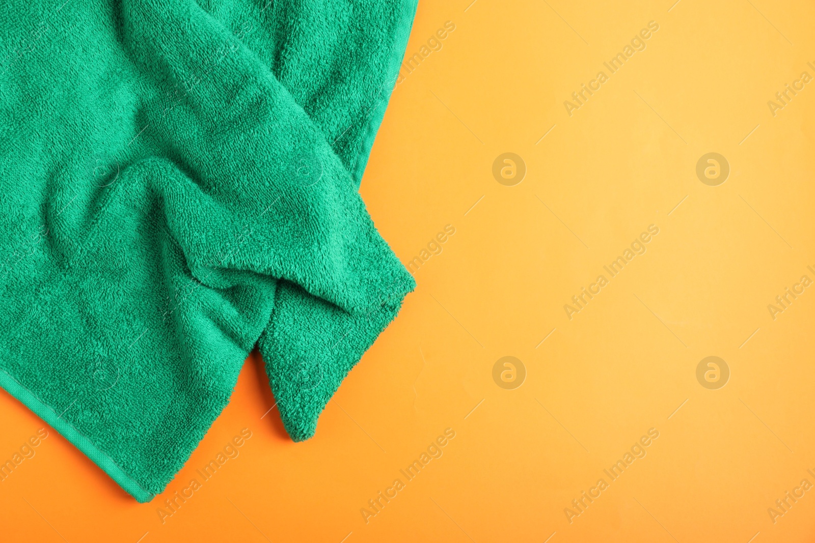 Photo of Green terry towel on orange background, top view. Space for text
