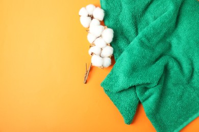 Photo of Green terry towel and cotton flowers on orange background, flat lay. Space for text