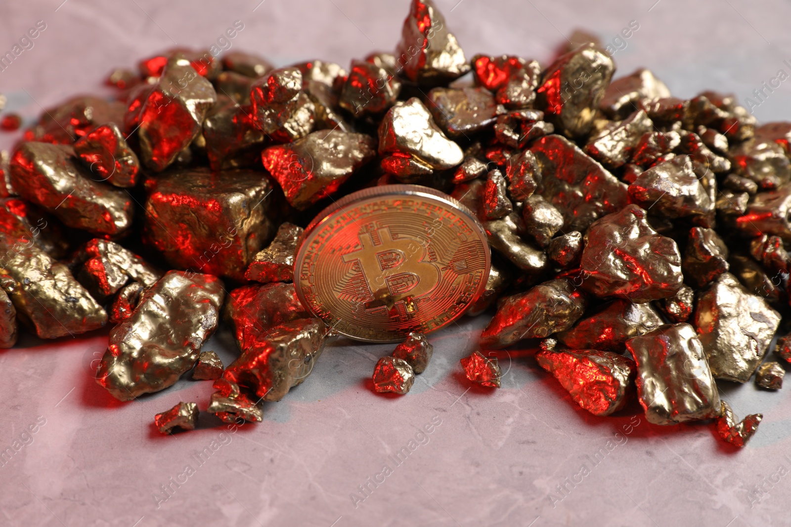 Photo of Bitcoin and gold nuggets on table in red light
