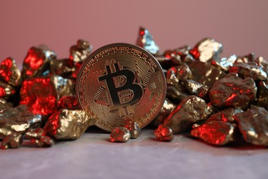 Photo of Bitcoin and gold nuggets on table in red light, closeup
