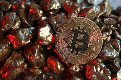 Photo of Bitcoin and gold nuggets on table in red light, closeup