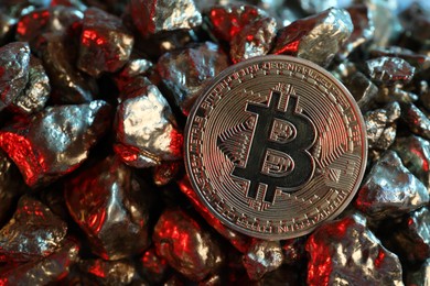Photo of Bitcoin and gold nuggets on table in red light, closeup