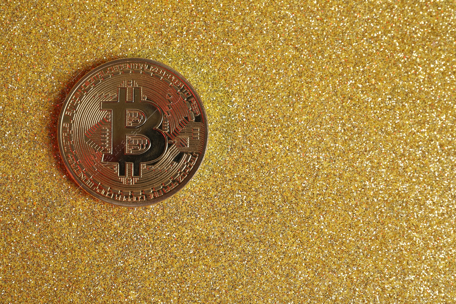 Photo of Bitcoin on golden glittery surface, top view. space for text