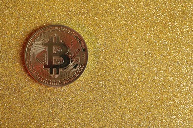 Photo of Bitcoin on golden glittery surface, top view. space for text
