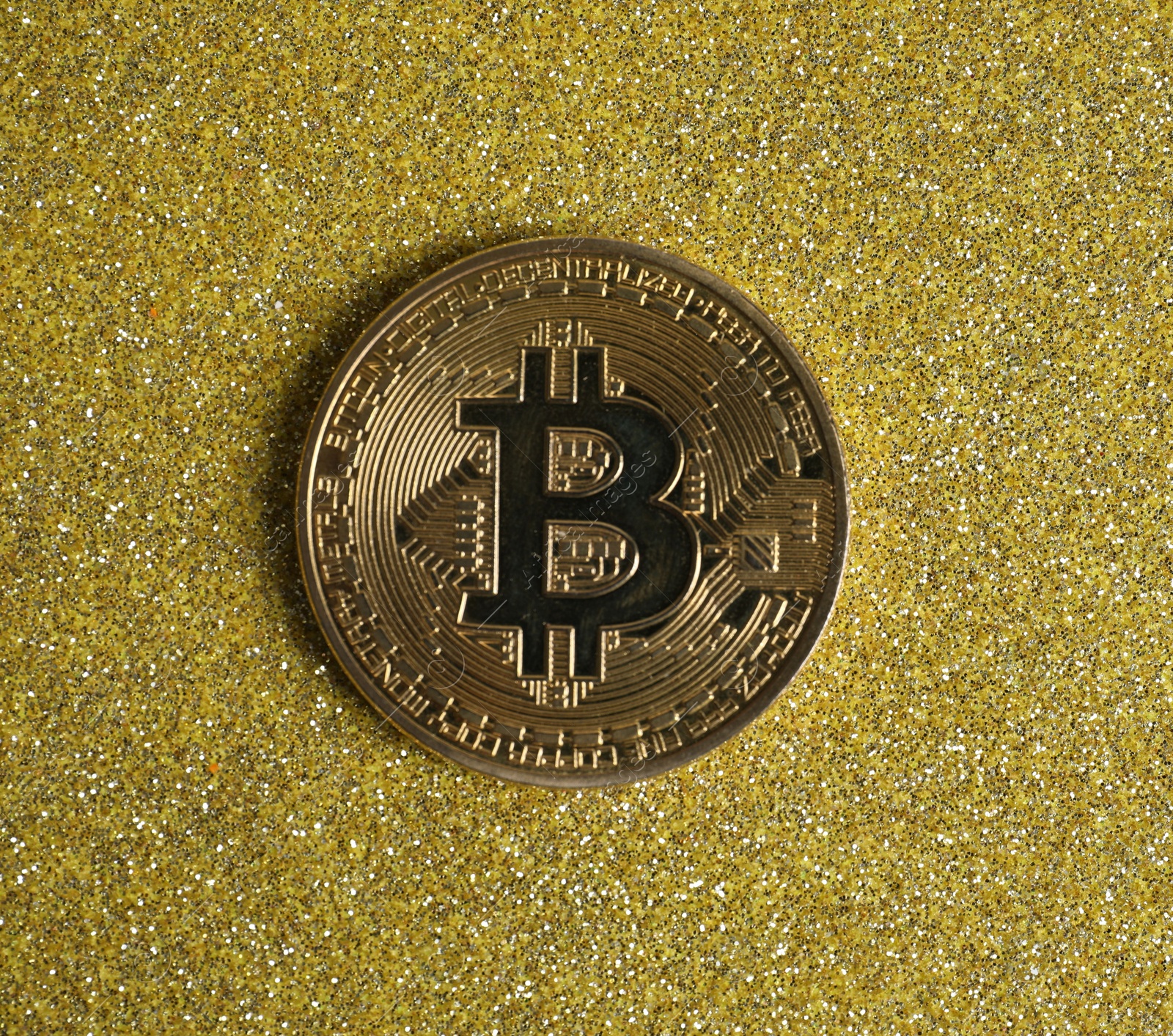 Photo of Bitcoin on golden glittery surface, top view