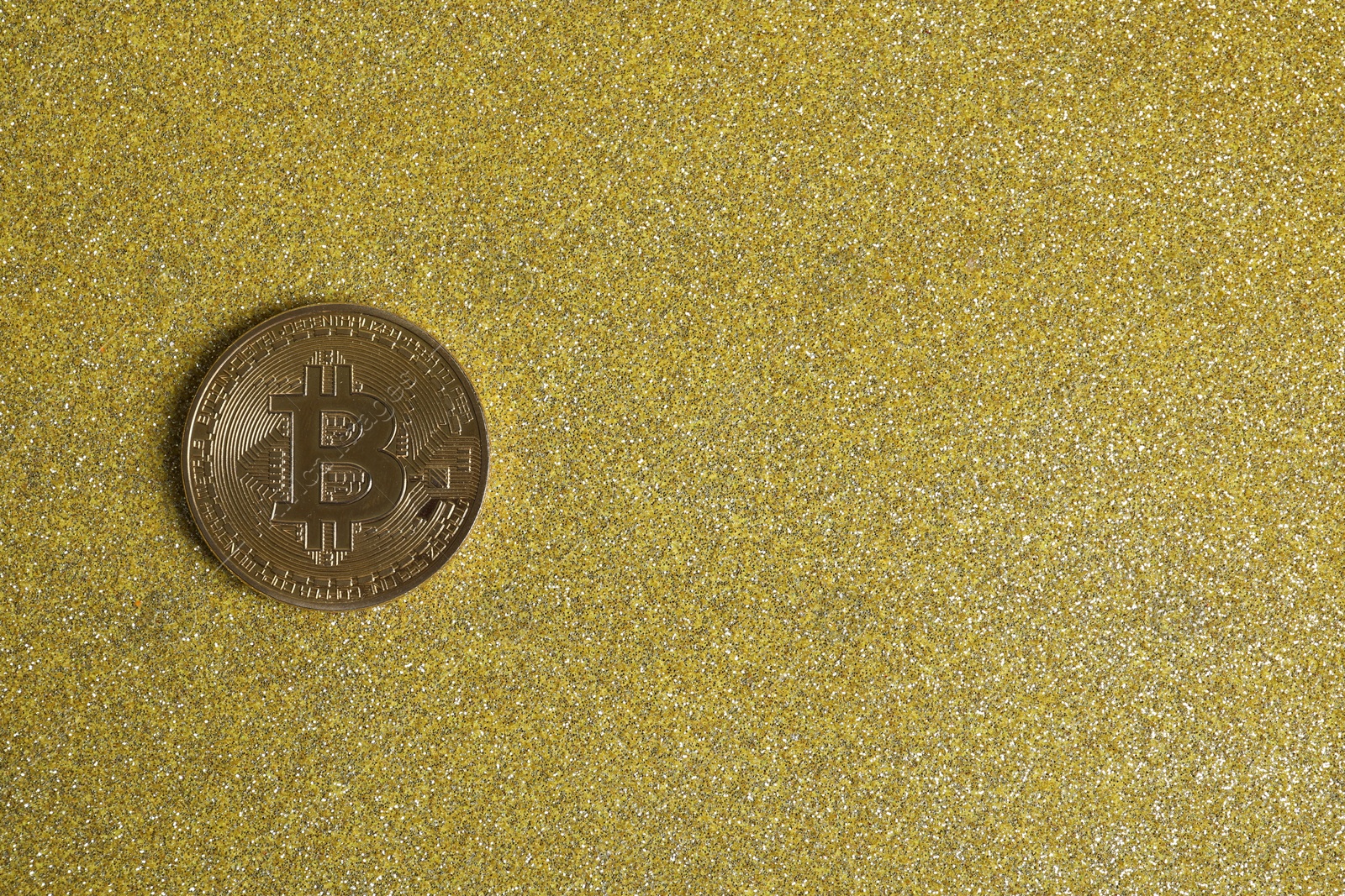 Photo of Bitcoin on golden glittery surface, top view. space for text