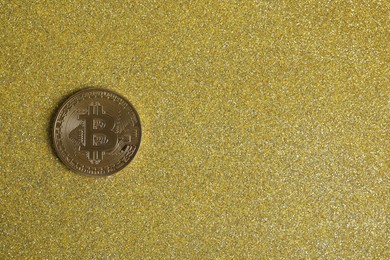 Photo of Bitcoin on golden glittery surface, top view. space for text