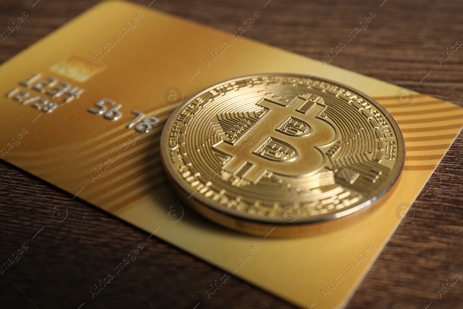 Photo of Bitcoin and plastic bank card on wooden table, closeup
