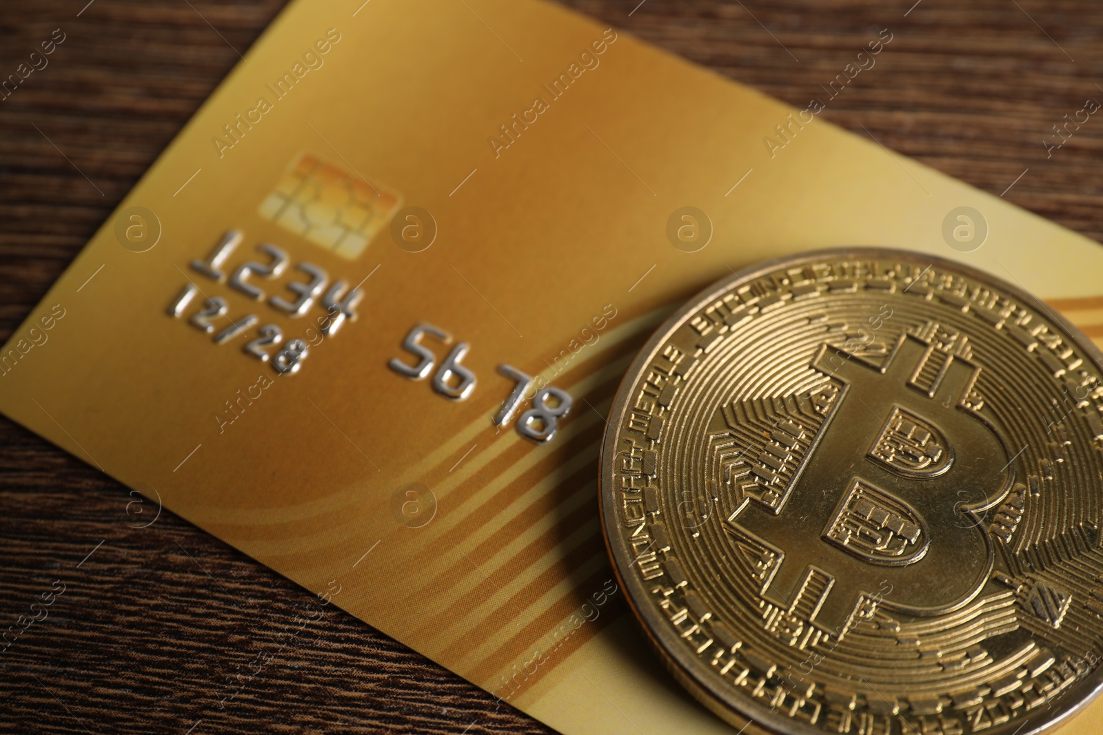 Photo of Bitcoin and plastic bank card on wooden table, closeup
