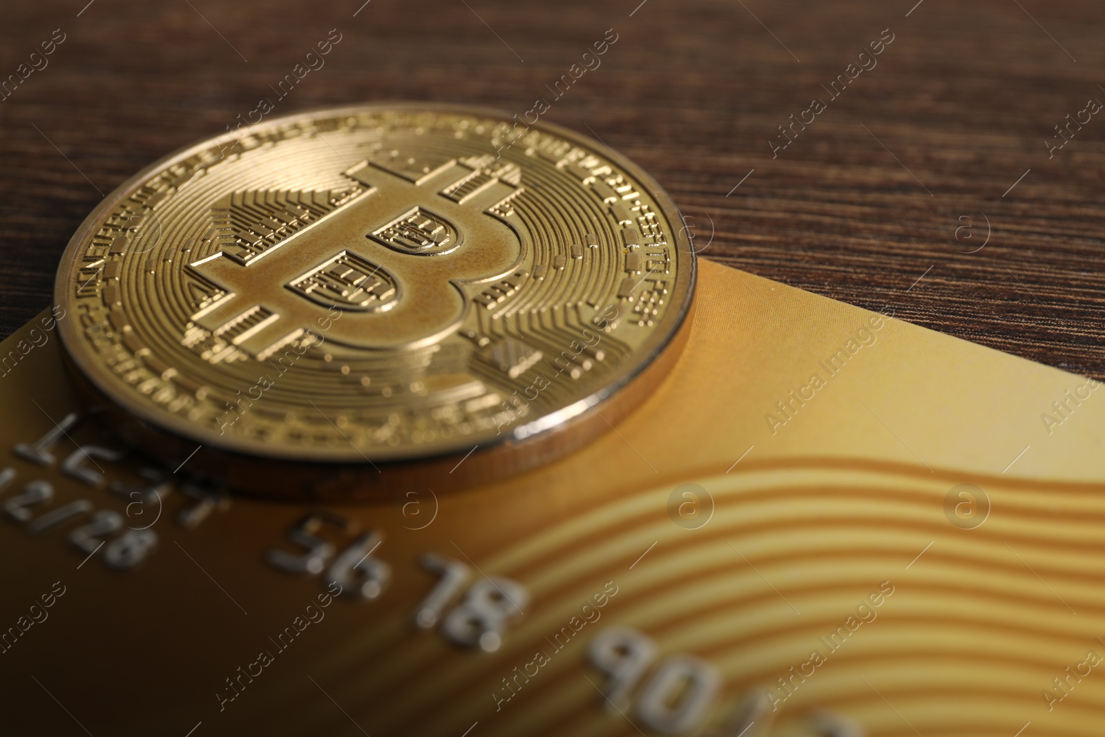 Photo of Bitcoin and plastic bank card on wooden table, closeup