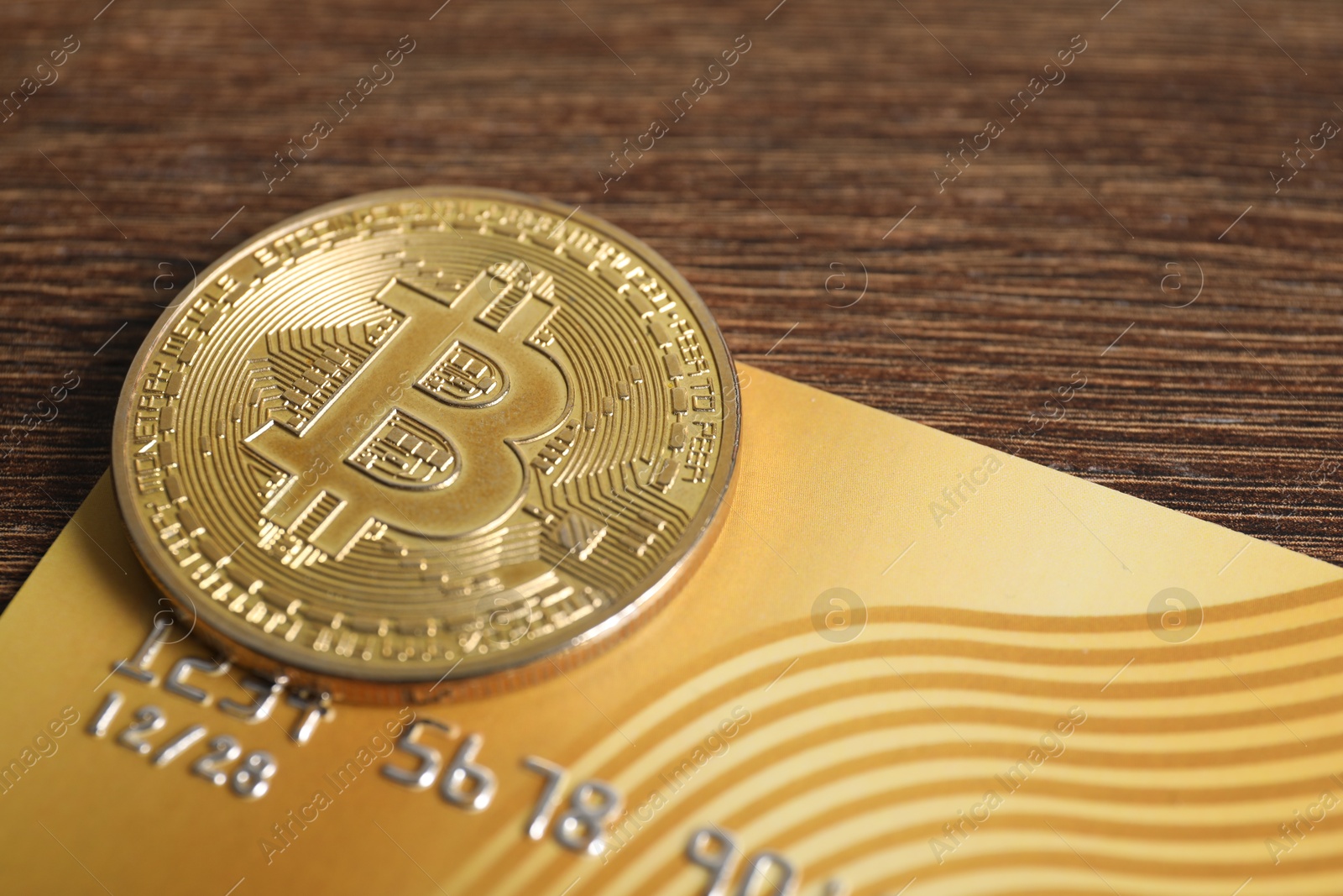 Photo of Bitcoin and plastic bank card on wooden table, closeup