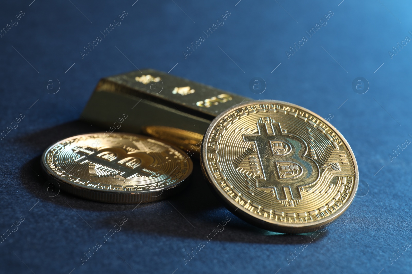 Photo of Bitcoins and gold bar on blue background, closeup