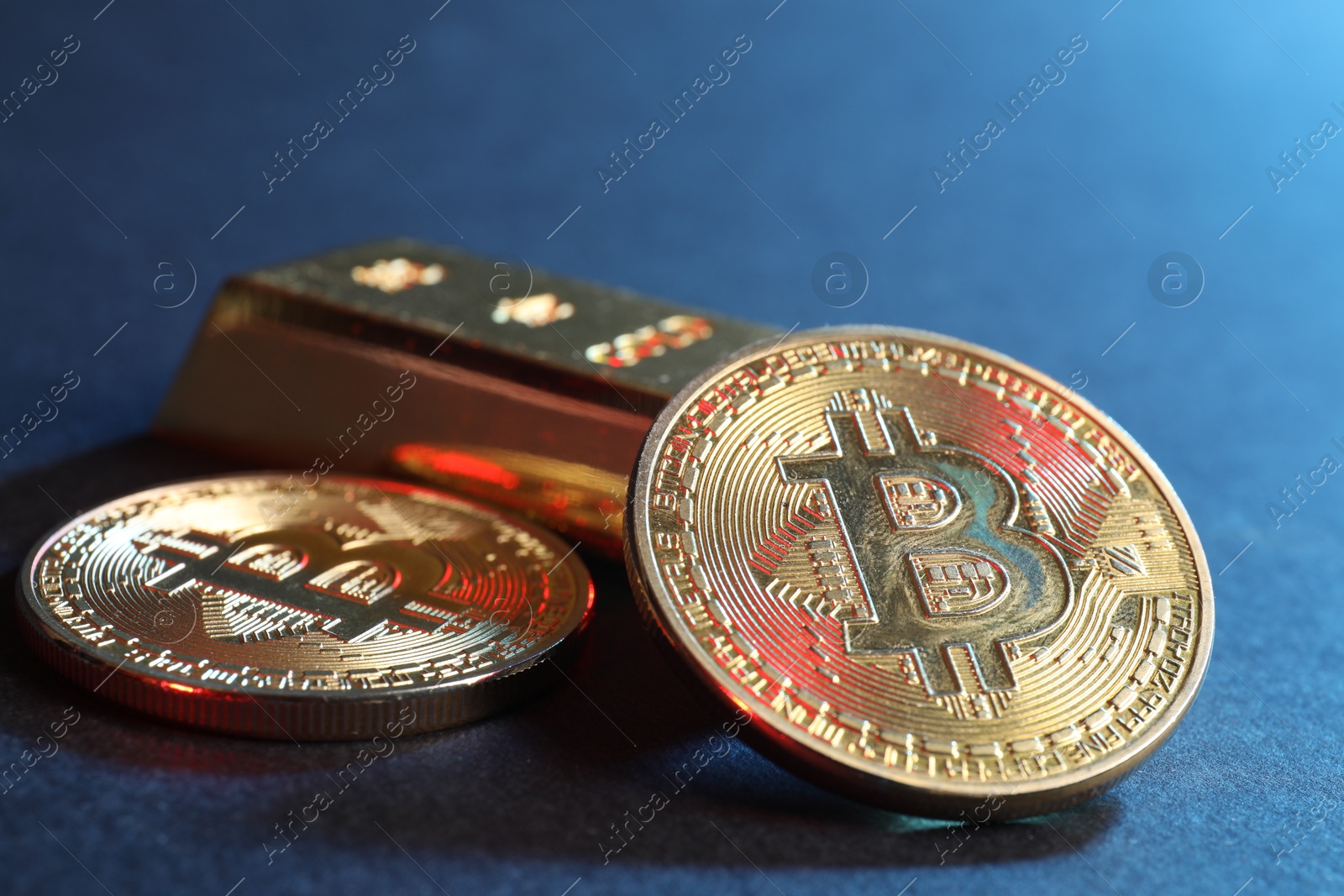 Photo of Bitcoins and gold bar on blue background, closeup