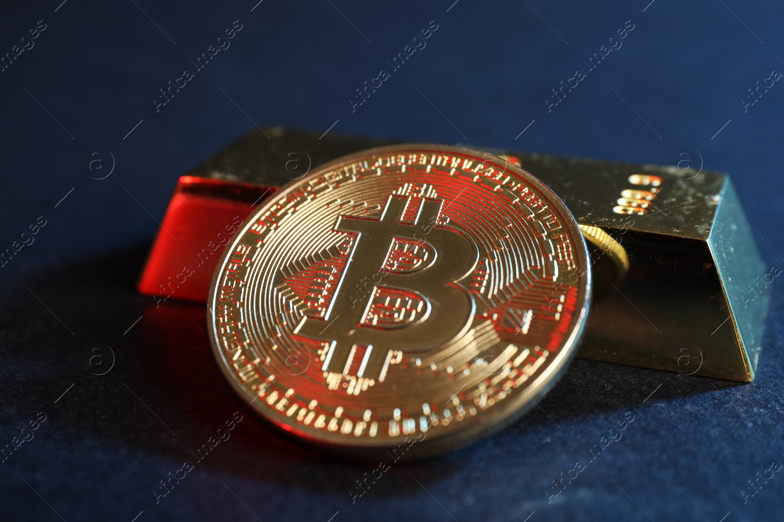Photo of Bitcoin and gold bar on blue background, closeup