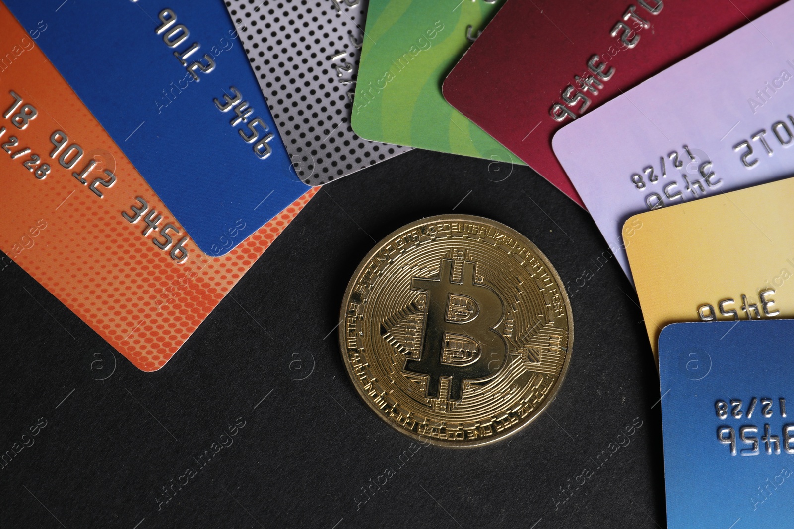Photo of Bitcoin and plastic bank cards on black background, flat lay